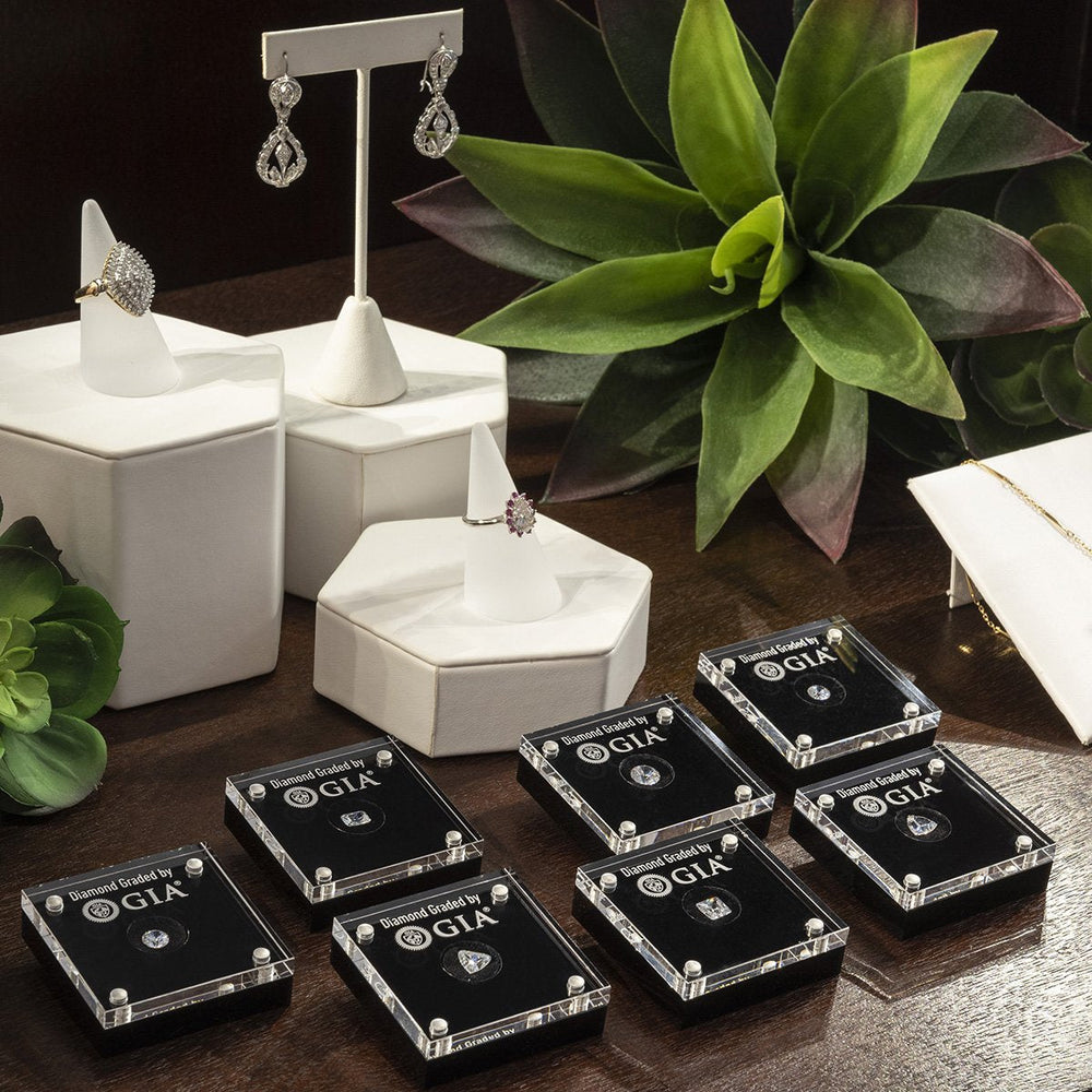 Group of 7 loose diamond display cases on counter with rings, earrings, and succulents